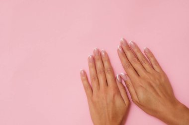 Pastel pembe arka planda Fransız manikürlü güzel kadınsı eller..