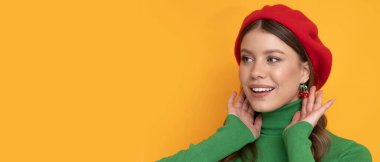 İzole edilmiş turuncu arka planda kırmızı bereli mutlu ve pozitif bir genç kadın..