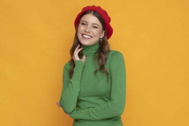 İzole edilmiş turuncu arka planda kırmızı bereli mutlu ve pozitif bir genç kadın..