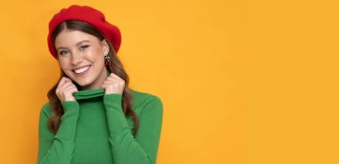 İzole edilmiş turuncu arka planda kırmızı bereli mutlu ve pozitif bir genç kadın..