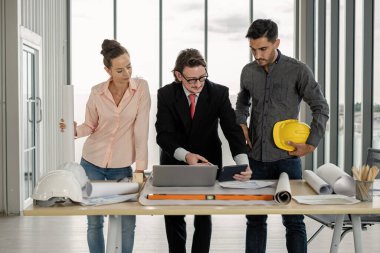 Erkek ve kadın mühendisler ve mimarlardan oluşan bir ekip, çalışma ekibi, inşaat planlarını tartışıyor ve çiziyor, baskı yapıyor, inşaat alanlarında yazıyor..