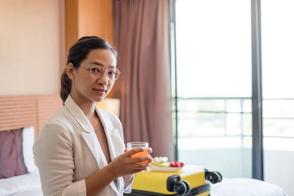An Asian businesswoman sits on a bed in a hotel room, exhausted from a business trip, ready to receive a fruit snack from the hotel, arranged for VIP guests.