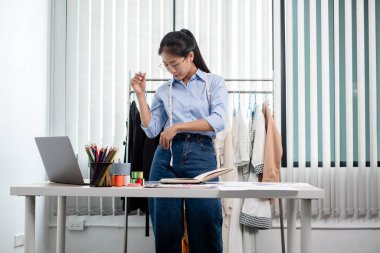 Tekstil aksesuarları ve girişimci tasarımcı çizimleriyle genç ve güzel Asyalı moda terzisi stüdyoda yaratıcı fikirler için dizüstü bilgisayarı olan parlak renklerle dolu..