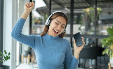Kulaklık takıp müzik dinleyen mutlu Asyalı kız akıllı telefondan dijital müzik dinlemenin tadını çıkarıyor. Rahatlama kavramları.