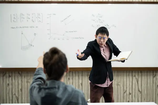 ホワイトボードの近くの教室では アジア系の男性教師が授業を作成し 授業のコラムで特別な講義を教えています 数学の先生は大学生への算術和を説明する — ストック写真