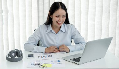 Bilgisayarda çalışan Asyalı kadın. Başarılı gülümseyen iş kadını ofiste çalışıyor ve notlar alıyor..