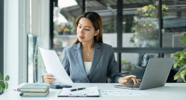 Asian businesswomen sit at their desks and calculate financial graphs showing results about their investments, planning successful business growth process.