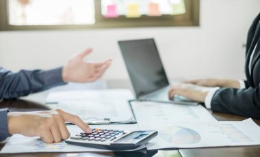 İki iş lideri çizelgeler, finansal grafikler hakkında konuşuyor. Sonuçları gösteren planlama stratejilerini analiz ediyor ve hesaplıyor. Ticari başarı oluşturma süreçlerini de..