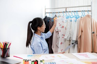 Tekstil aksesuarları ve girişimci tasarımcı çizimleriyle genç ve güzel Asyalı moda terzisi stüdyoda yaratıcı fikirler için dizüstü bilgisayarı olan parlak renklerle dolu..