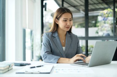 Asyalı iş kadını masalarında oturup yatırımlarıyla ilgili sonuçları gösteren finansal grafikleri hesaplıyor ve başarılı bir iş büyüme süreci planlıyor.