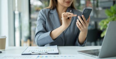 Asyalı iş kadını masalarında oturup yatırımlarıyla ilgili sonuçları gösteren finansal grafikleri hesaplıyor ve başarılı bir iş büyüme süreci planlıyor.