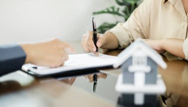 Ev modeli olan bir emlakçı, ev sigortası yaptırmak ve resmi pazarlıklar tamamlandıktan sonra sözleşmeyi imzalamak için müşterilerle görüşüyor..