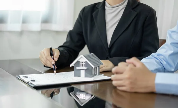 A real estate agent with a home model is talking to clients about renting a house buying home insurance and contracting the contract after the formal negotiation is completed.