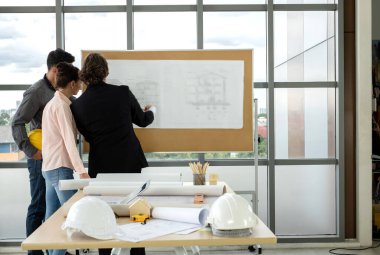 Erkek ve kadın mühendisler ve mimarlardan oluşan bir ekip, çalışma ekibi, inşaat planlarını tartışıyor ve çiziyor, baskı yapıyor, inşaat alanlarında yazıyor..