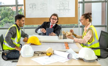 Erkek ve kadın mühendisler ve mimarlardan oluşan bir ekip, çalışma ekibi, inşaat planlarını tartışıyor ve çiziyor, baskı yapıyor, inşaat alanlarında yazıyor..