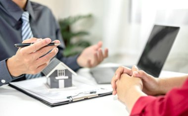 Ev modeli olan bir emlakçı ev sigortası almak için müşterilerle konuşuyor. Ev sigortası kavramı.