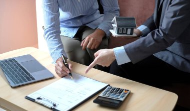 Ev modeli olan bir emlakçı, müşterilerle ev sigortası satın almak ve resmi sözleşme altında müşterilere sözleşme imzalatmak hakkında konuşuyor. Ev kiralama ve sigorta konsepti.