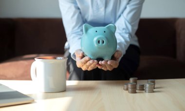 Kumbarası olan ve tasarruf masasına madeni para koyan genç bir kadın büyüyen işi başarı ve emeklilik için arttırıyor..