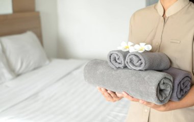 Bir otel hizmetçisi yataktaki havluları istifledi ve otel odasındaki havluların üzerine çiçekler koydu..