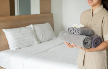 Bir otel hizmetçisi yataktaki havluları istifledi ve otel odasındaki havluların üzerine çiçekler koydu..