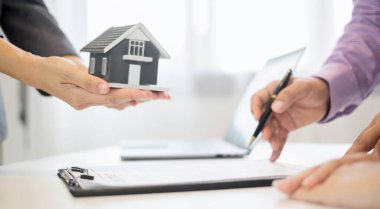 Ev modeli olan bir emlakçı ev sigortası almak için müşterilerle konuşuyor. Ev sigortası kavramı.