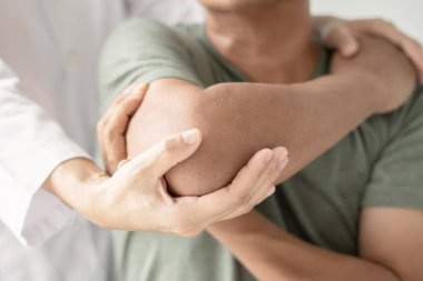 Kadın fizyoterapistler, dirsek yaralanması olan erkek hastalara rehabilitasyon merkezlerindeki hastaları muayene etmede yardımcı oluyorlar. Fizyoterapi kavramları.