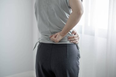 Uzun süre sırt ağrısı çeken bir kadın. Ofiste sıkı çalışırken rahatlamak ve dinlenmek için esnemek..