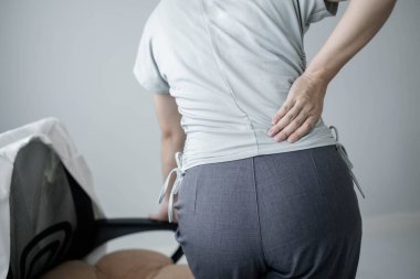 Uzun süre sırt ağrısı çeken bir kadın. Ofiste sıkı çalışırken rahatlamak ve dinlenmek için esnemek..