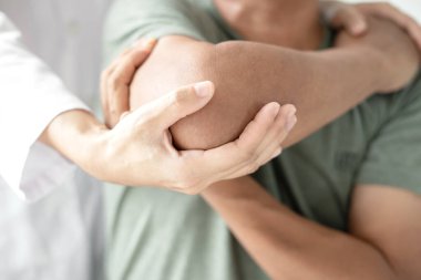 Kadın fizyoterapistler, dirsek yaralanması olan erkek hastalara rehabilitasyon merkezlerindeki hastaları muayene etmede yardımcı oluyorlar. Fizyoterapi kavramları.