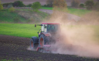 İlkbaharda kırmızı traktör sürüşü, traktördeki tarla sürüşü tarlaları hazırlayan çiftçi, tarım arazilerindeki tarım işleri, traktör manzarası.