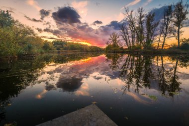 Gün batımı saatinde güneş ile yaz başında doğal nehir. Renkli bulutların yansımaları ile sakin su. Macaristan
