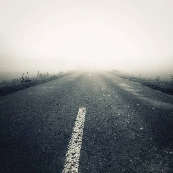 Sisin içinde boş bir yol var. Sonbahar mevsiminde sisli asfalt yol.