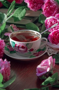 Pembe kokulu güllerle çevrili bir fincan çay..