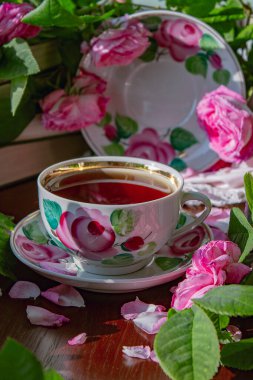 Pembe kokulu güllerle çevrili bir fincan çay..