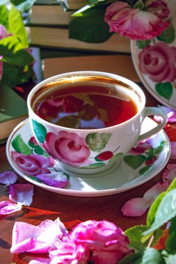 Pembe kokulu güllerle çevrili bir fincan çay..