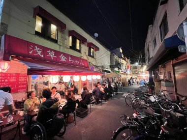 Tokyo - 4 Mayıs 2023: Ziyaretçiler geceleri hobi caddesinde sokak yemeklerinin tadını çıkarıyorlar. Gece yarısı bir restoran sokağında.