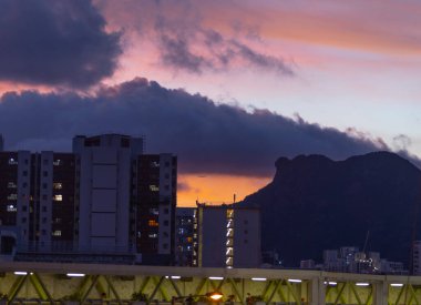 Kowloon 'un ünlü simgesi Lion Rock Dağı, sağ tarafta ve günbatımının arka planında yer almaktadır. logo kaldırıldı