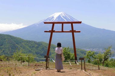 a girl pray in front of a traditional red Torii gate with the landscape of Mt. Fuji   clipart