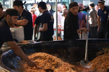 Taşkent, Özbekistan - Ekim 12024: şef mutfakta pilav ya da pilav ateşledi. Plov, Orta Asya 'da genellikle stok ve et suyunda pişirme ve baharat içeren ünlü bir yemektir.