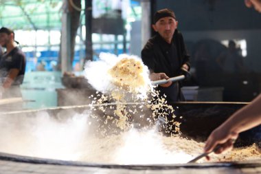 Taşkent, Özbekistan - Ekim 12024: şef mutfakta pilav ya da pilav ateşledi. Plov, Orta Asya 'da genellikle stok ve et suyunda pişirme ve baharat içeren ünlü bir yemektir.
