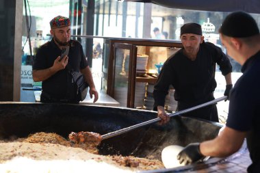 Taşkent, Özbekistan - Ekim 12024: şef mutfakta pilav ya da pilav ateşledi. Plov, Orta Asya 'da genellikle stok ve et suyunda pişirme ve baharat içeren ünlü bir yemektir.