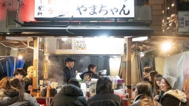  Fukoka, Japonya- 18 Ocak 2024: İnsanlar Yatai Gıda Dükkanlarında yemek yiyor. Yatai Gıda Dükkanları her akşam şehrin dört bir yanında geçici gıda tezgahları kuruyor ve yerli halk ve ziyaretçilerden oluşan kalabalıklar toplanıyor.