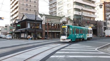 Kumamoto, Japonya - 15 Ocak 2025: Nagasaki Jiro Kissa Shitsu adlı eski kahve dükkanından tramvay geçişi. Kumamoto 'nun tarihi ve geleneksel kafelerinden biridir..