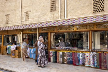 Buhara, Özbekistan - 2 Ekim 2024: Poi-Kalyan duvarı yakınındaki kumaş mağazası ürünü turistlere satıyor.