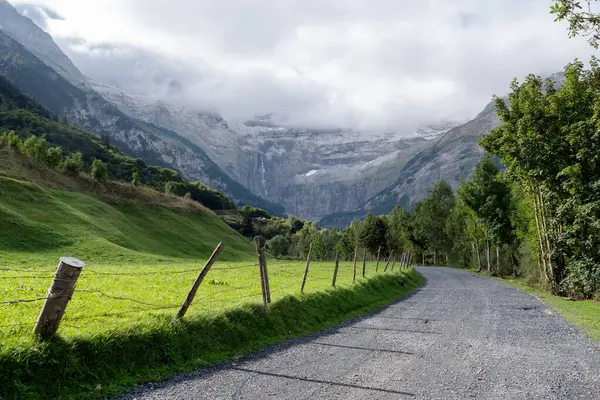 Gavarnie Sirki, Fransız Pyrenes Dağları. Dağlar karla kaplı ve gökyüzü bulutlu. Nehir yemyeşil bir vadiyle çevrilidir.