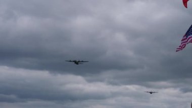 Arka planda büyük bir Amerikan bayrağıyla gökyüzünde uçan iki uçak.