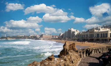 Kayalık bir kıyı şeridi ve iskelesi olan bir Biarritz plajı. Gökyüzü bulutlu ve su dalgalı.