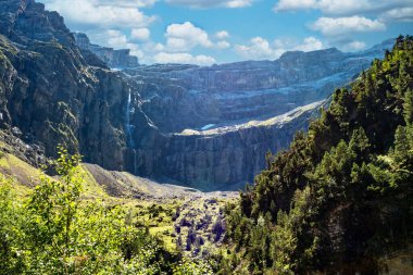 Gavarnie Sirki, Fransız Pyrenes Dağları. Dağlar karla kaplı ve gökyüzü bulutlu. Nehir yemyeşil bir vadiyle çevrilidir.