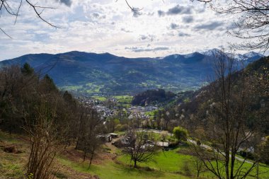 Aşağıdaki vadide bir kasabası olan bir dağ sırası. Gökyüzü bulutlu ve güneş bulutların arasında parlıyor.
