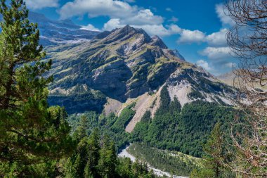 İçinden nehir akan bir dağ sırası. Gökyüzü mavi ve dağlar ağaçlarla kaplı.